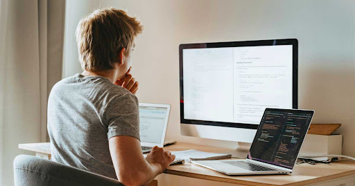 Man sitting at a desk coding a chatbot on multiple screen displays