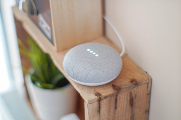 A Google Home Mini sits on a wooden shelf