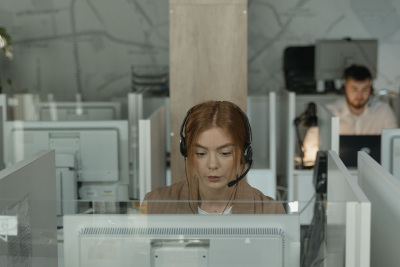 woman at a computer at a help center alt= A woman wearing a headset is working in a call center.